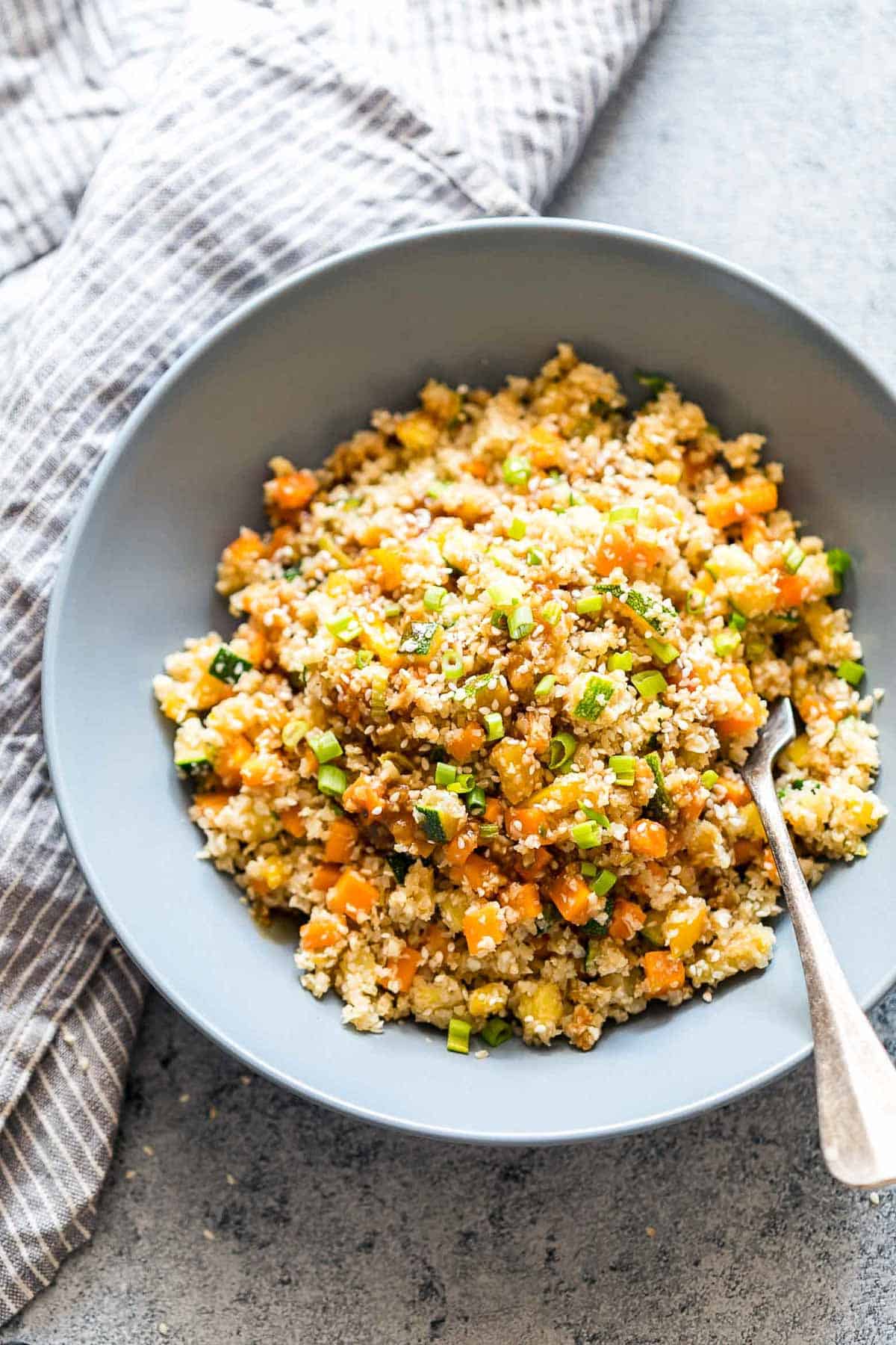 Low Carb Asian Cauliflower Rice topped with sesame seeds, chopped green onions and served in a bowl.