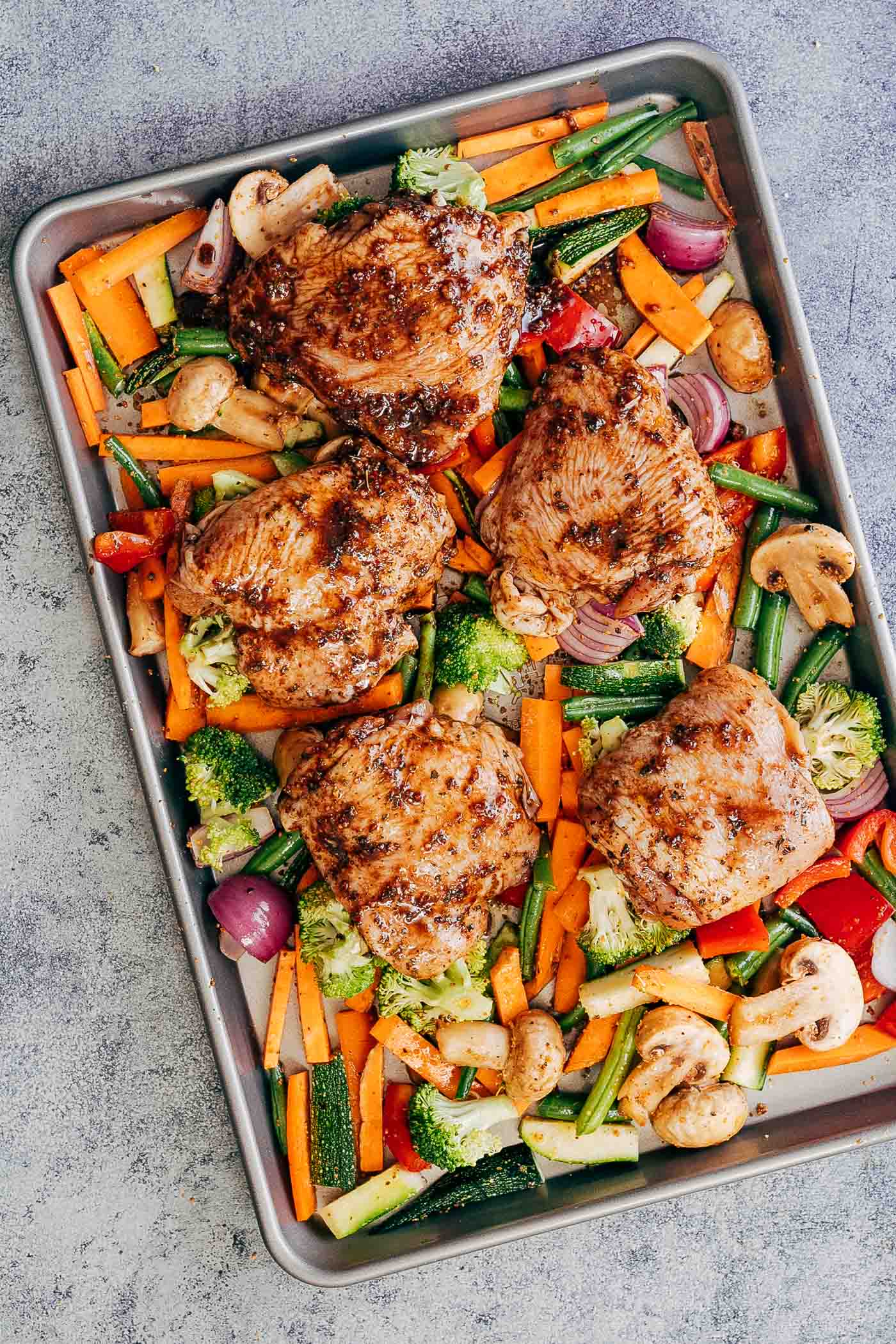 Marinated sheet pan honey balsamic chicken thighs with veggies on a baking tray ready to go into the oven