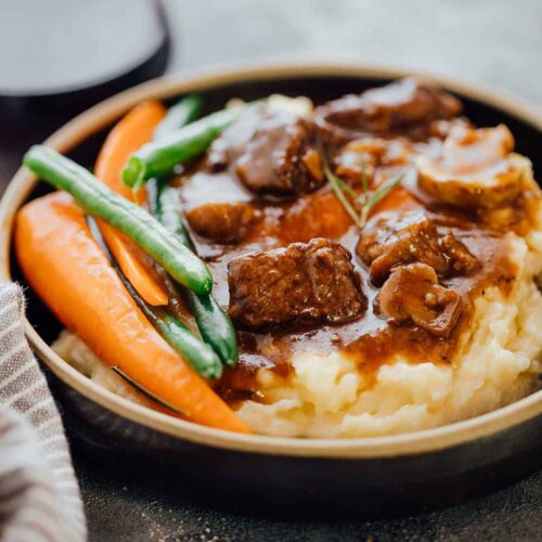Pressure Cooker Beef Bourguignon served with mashed potatoes and grilled veggies in a black plate.