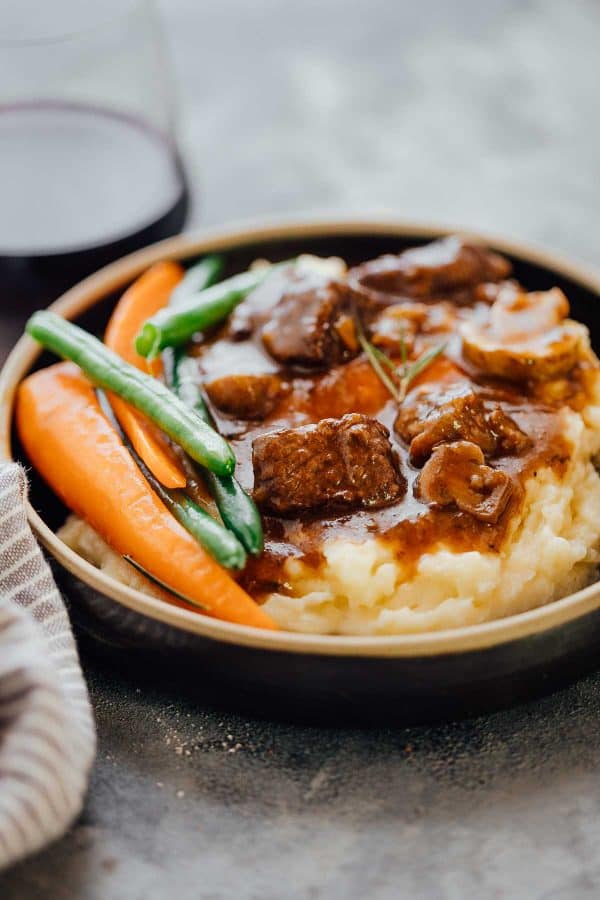 Beef Bourguignon made in a pressure cooker and served over mashed potatoes with green beans and carrots on the side