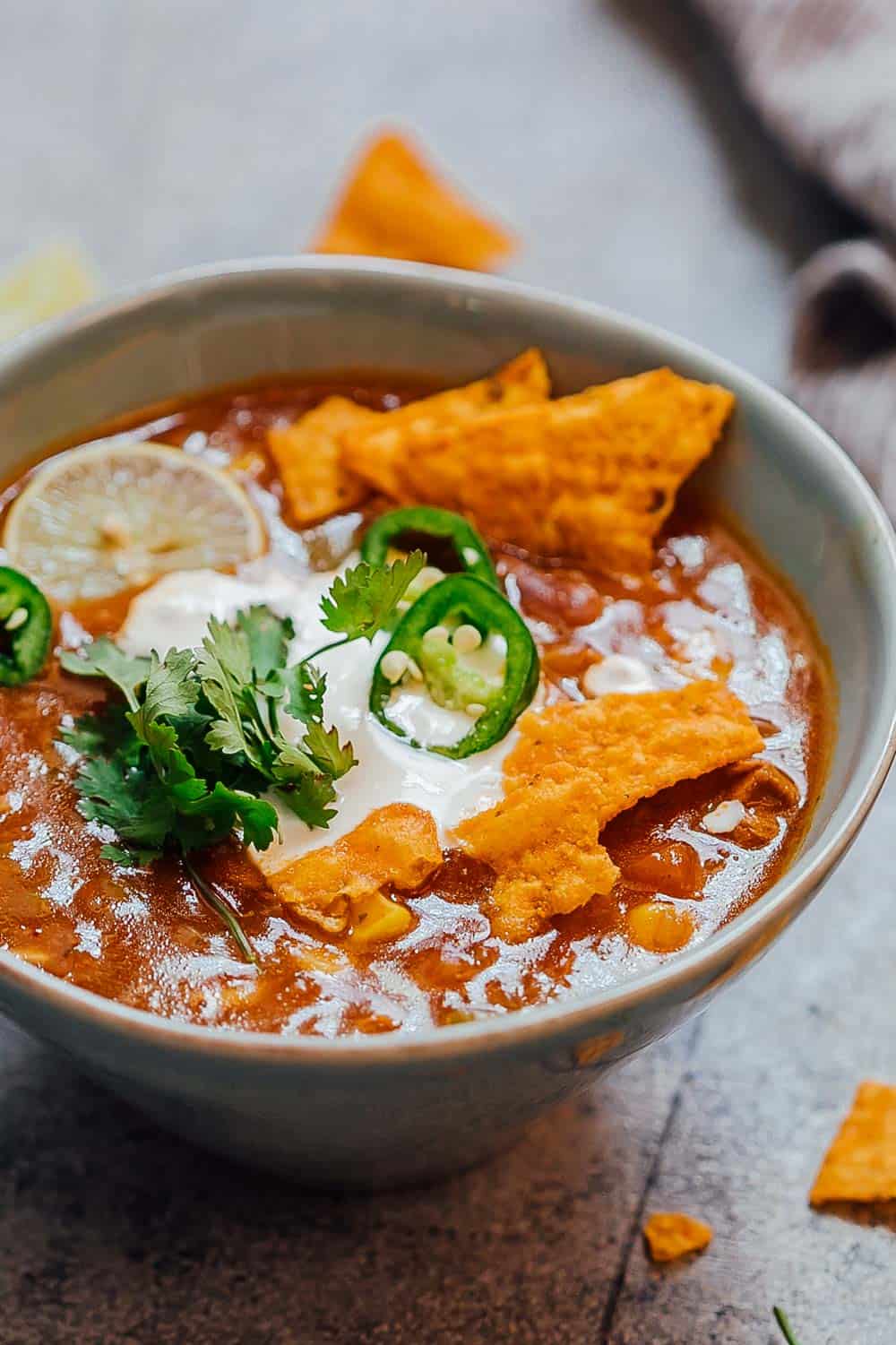 Bowl of chicken enchilada soup made in the Instant Pot topped with sour cream, cilantro, sliced jalapenos, tortilla chips and a lime wedge