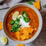 Bowl of yellow enchilada soup made in the Instant Pot topped with sour cream, cilantro, sliced jalapenos, tortilla fries and a lime wedge