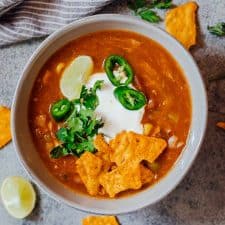Bowl of chicken enchilada soup made in the Instant Pot topped with sour cream, cilantro, sliced jalapenos, tortilla chips and a lime wedge