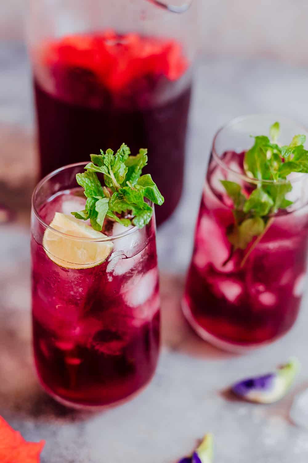 Closeup of a glass of hibiscus tea with ice cubes, mint and lemon