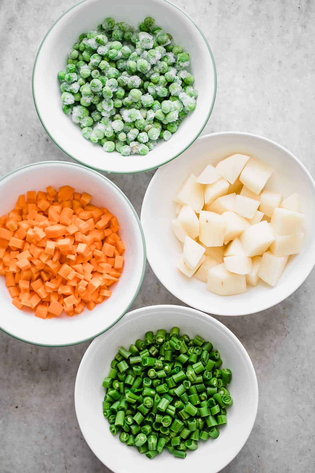 Mise en place for pressure cooker veg pulao. Pcture of frozen green peas, carrots, beans and potatoes n bowls all ready to go into the recipe