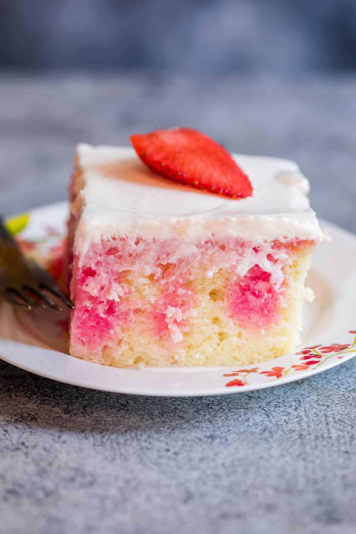 Closeup of a slice of a strawberry poke cake with drizzles of jello visible through the cake. 