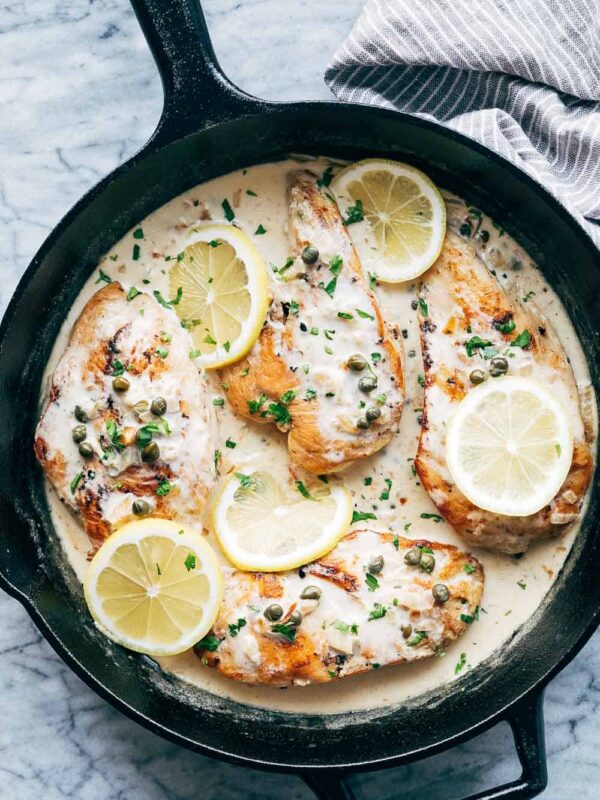 Creamy lemon chicken scallopini served in a cast iron skillet with four chicken breasts with capers and lemons on top
