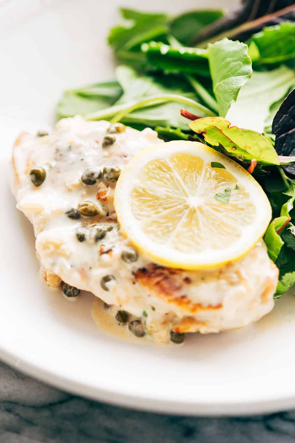 Creamy lemon chicken scallopini served with a light salad on the side in a white bowl