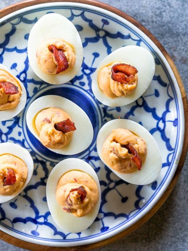 Spicy bacon deviled eggs on a blue and white plate topped with bacon