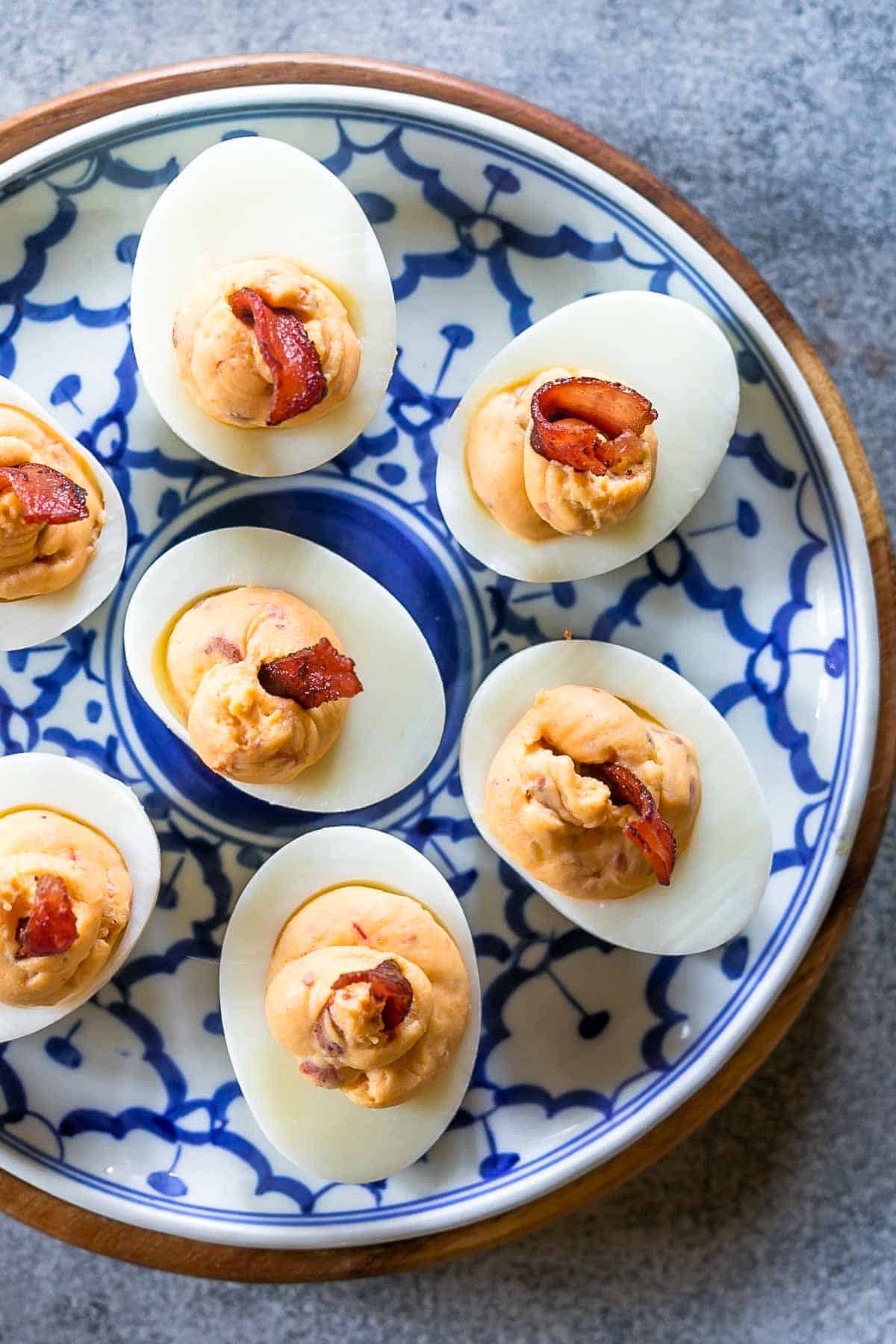 Spicy bacon deviled eggs on a blue and white plate topped with bacon