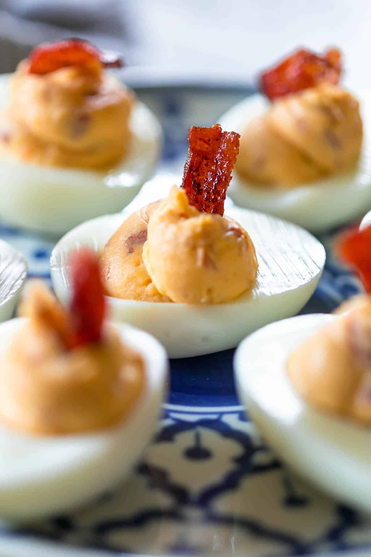Close up of Spicy bacon deviled eggs on a blue and white plate topped with bacon