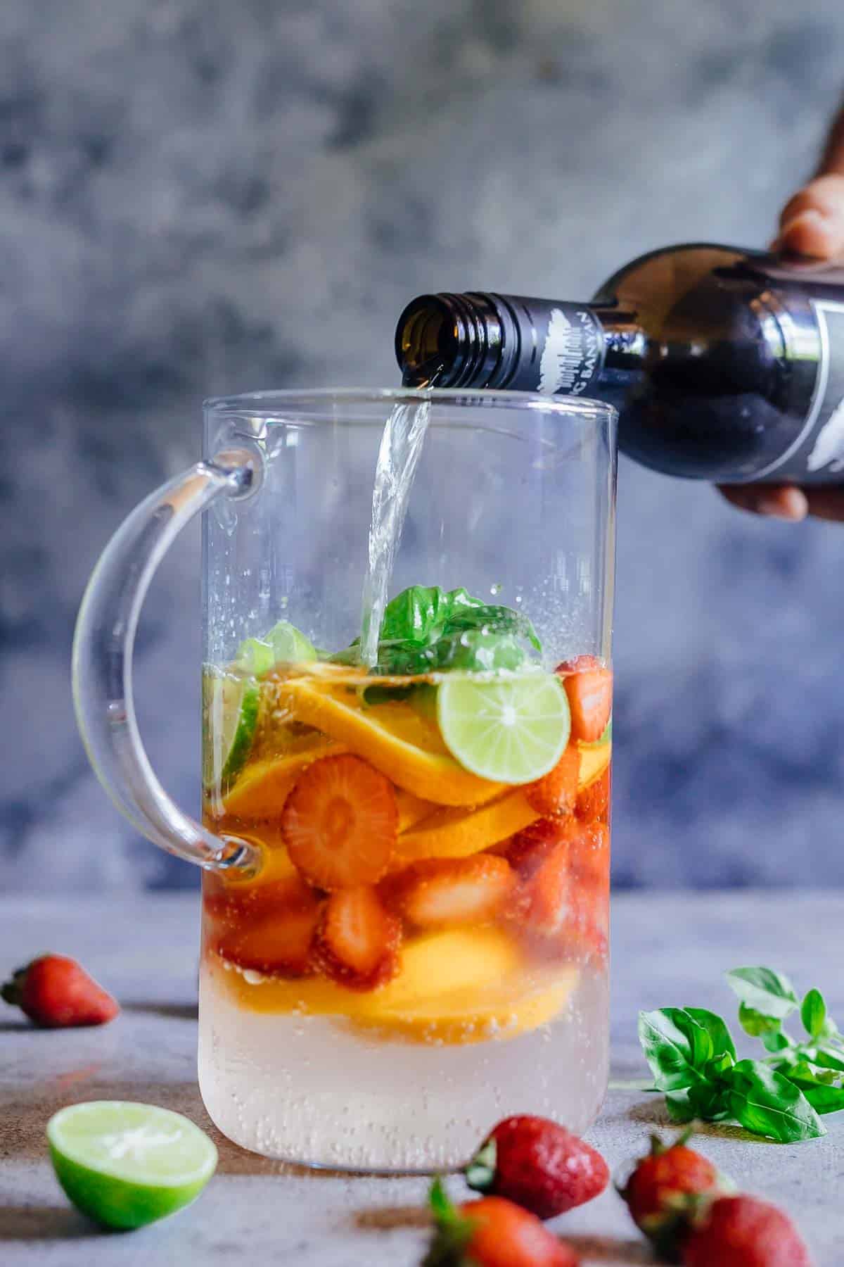 Pouring wine in a pitcher over fruits to make Strawberry Orange White Wine Sangria
