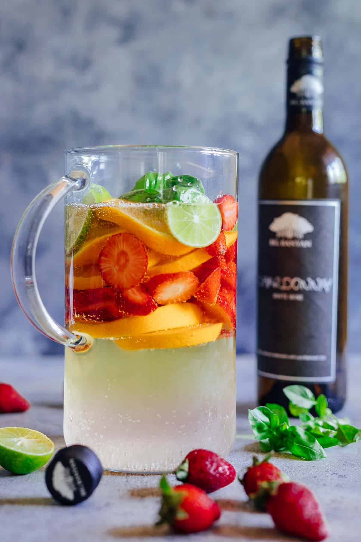 A pitcher of strawberry orange white wine sangria with a bottle of chardonnay in the background