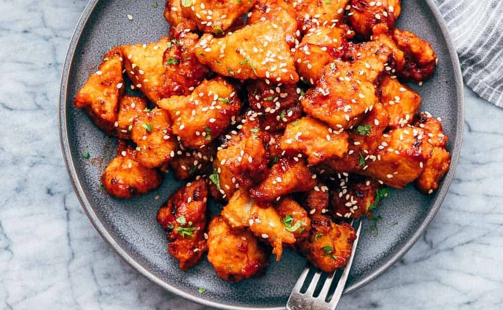 Korean Popcorn Chicken on a plate with a hand coming up to take a bite with a fork