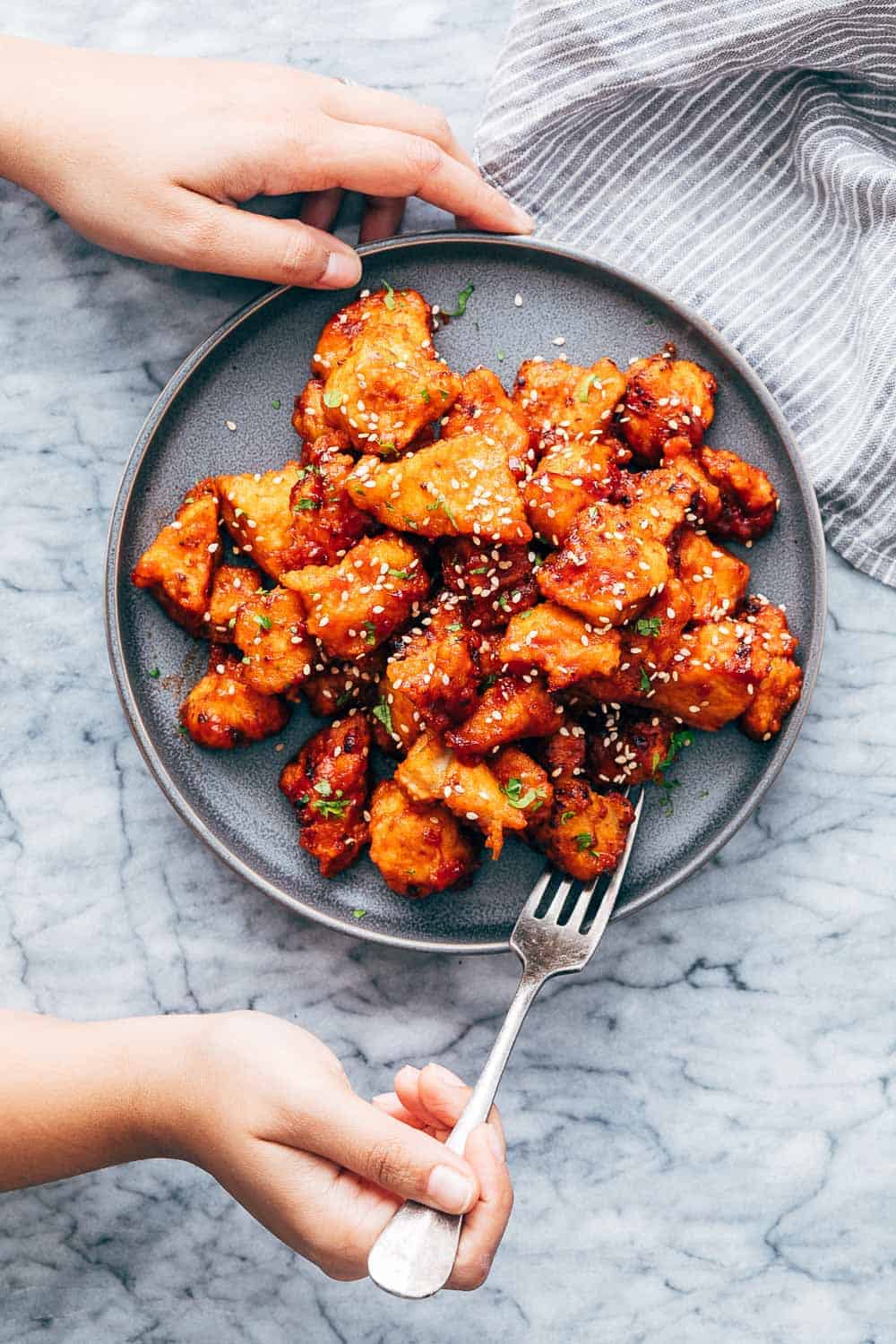 Korean Popcorn Chicken on a plate with a hand coming up to take a bite with a fork