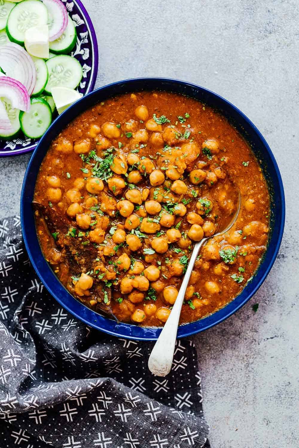 Pressure cooker chana masala in a blue bowl with cucumbers, onions etc on the side