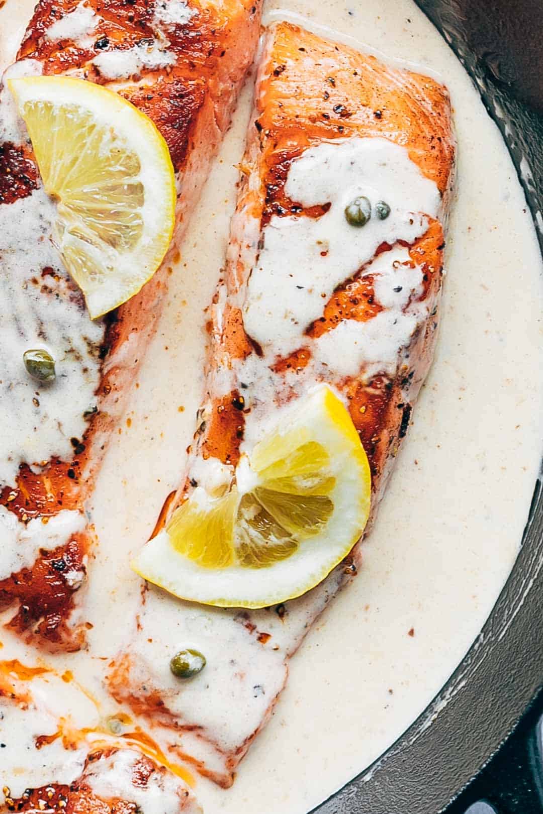 Close up of creamy salmon piccata with lemon sauce on top in a pan