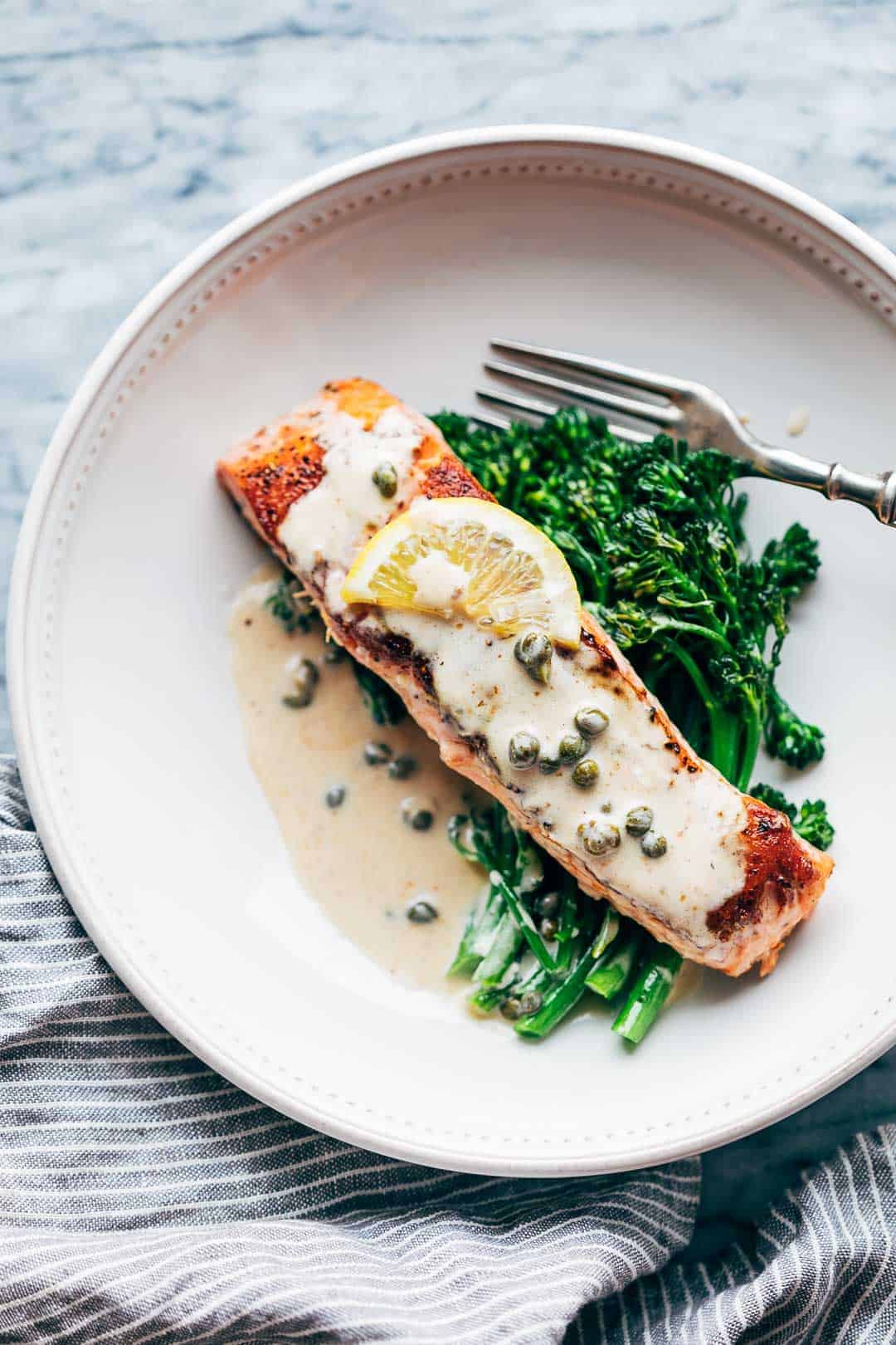 Creamy salmon piccata with lemon butter sauce served with steamed broccolini in a white bowl