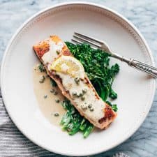 Creamy Salmon Piccata with creamy Lemon Sauce served with greens on a white plate.