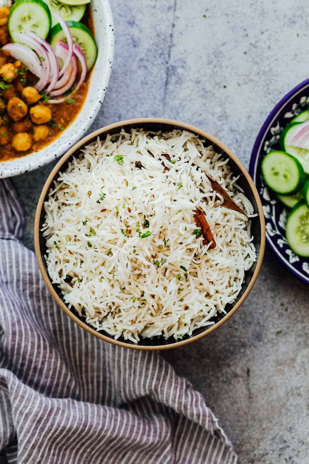 Jeera Rice served in a bowl with curry and salad on the side