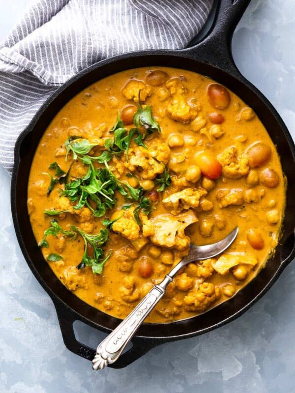 Cauliflower Chickpea Coconut Curry straight from the stove to the table in a cast iron skillet with a spoon