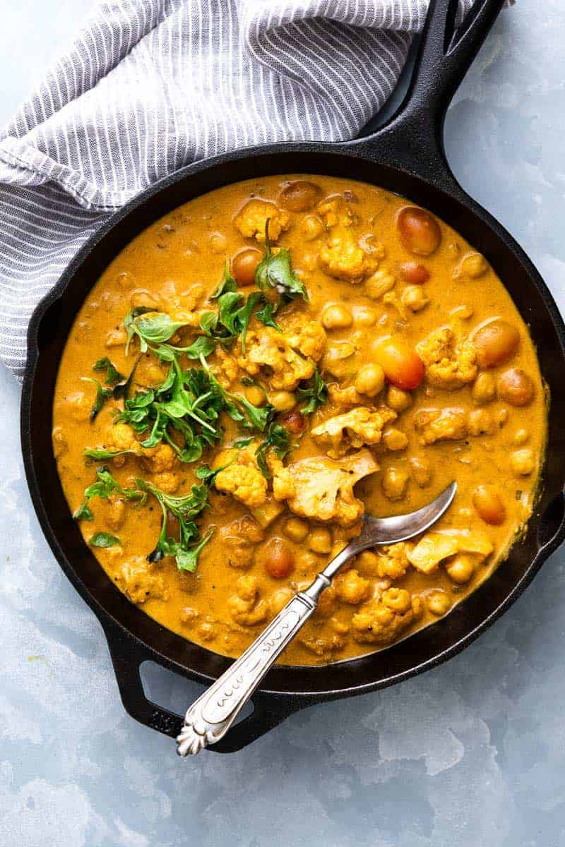 Cauliflower Chickpea Coconut Curry straight from the stove to the table in a cast iron skillet with a spoon