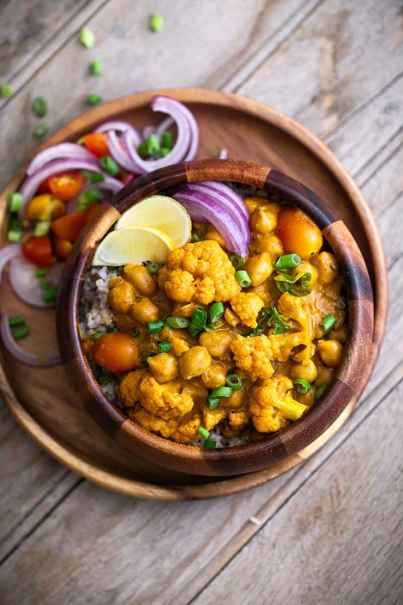 Cauliflower Chickpea Coconut Curry served in a brown bowl with onions and lime wedges