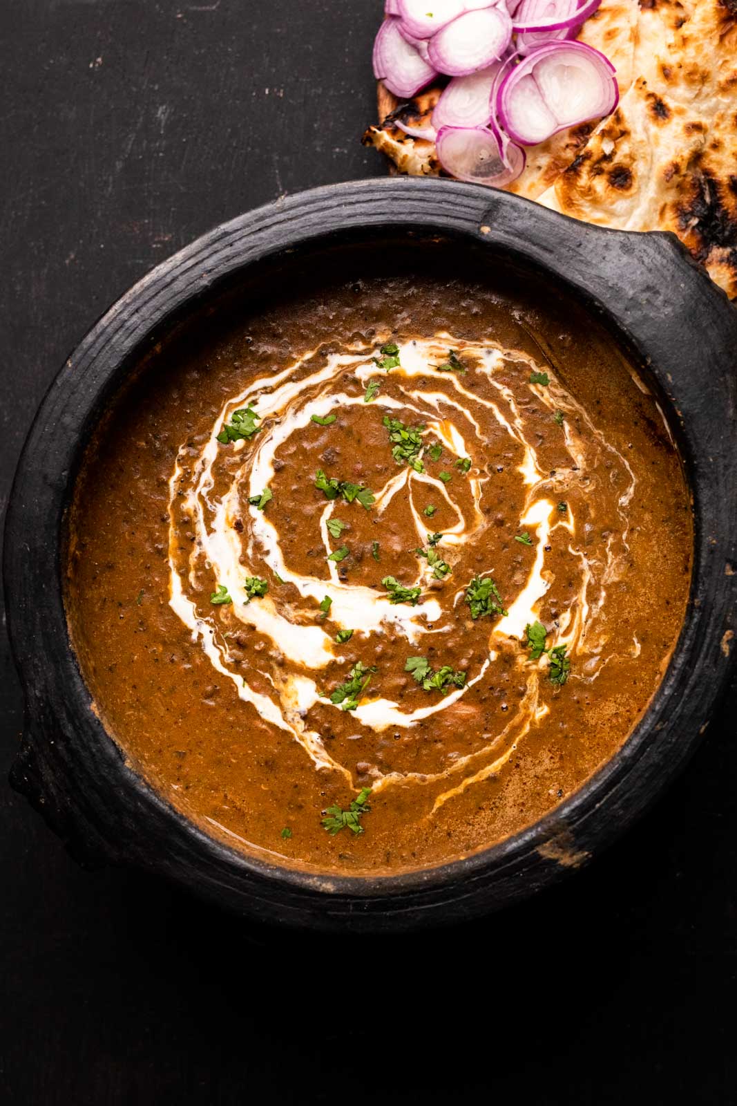 Indian Dal Makhani served in a mud pot it was cooked in, with cream drizzled on top