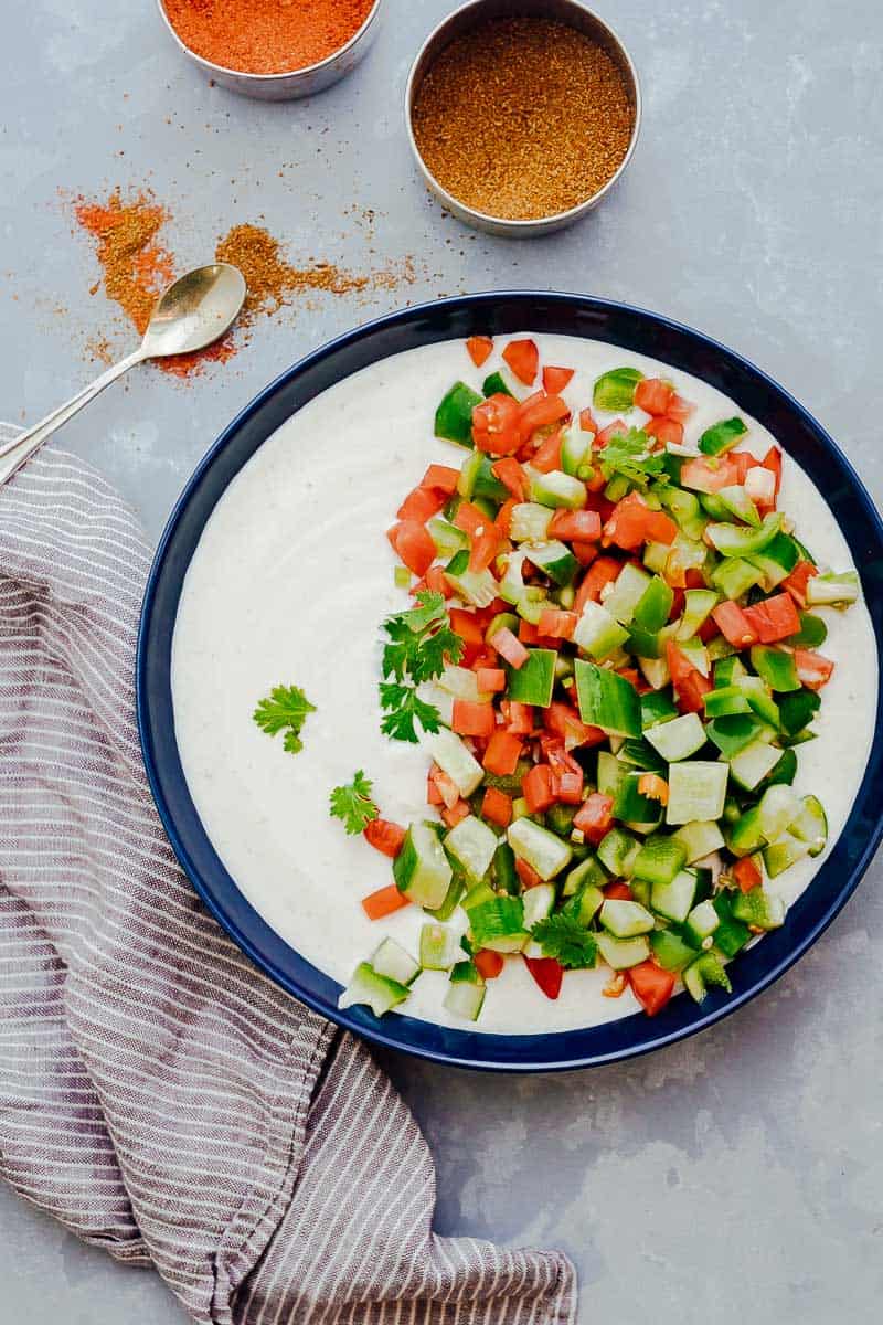 Chopped tomato, cucumber, onions and cilantro being mixed into a bowlful of whisked yogurt