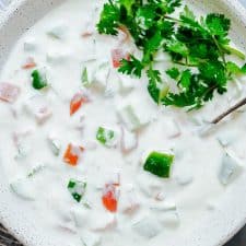 Closeup of Indian raita served in a white bowl topped with coriander or cilantro.