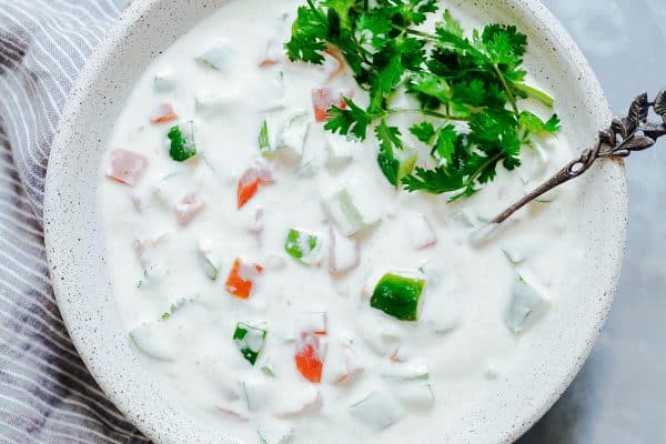 Closeup of Indian raita served in a white bowl topped with coriander or cilantro.