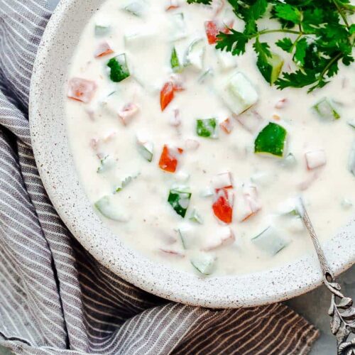 Indian raita served in a white bowl topped with coriander or cilantro