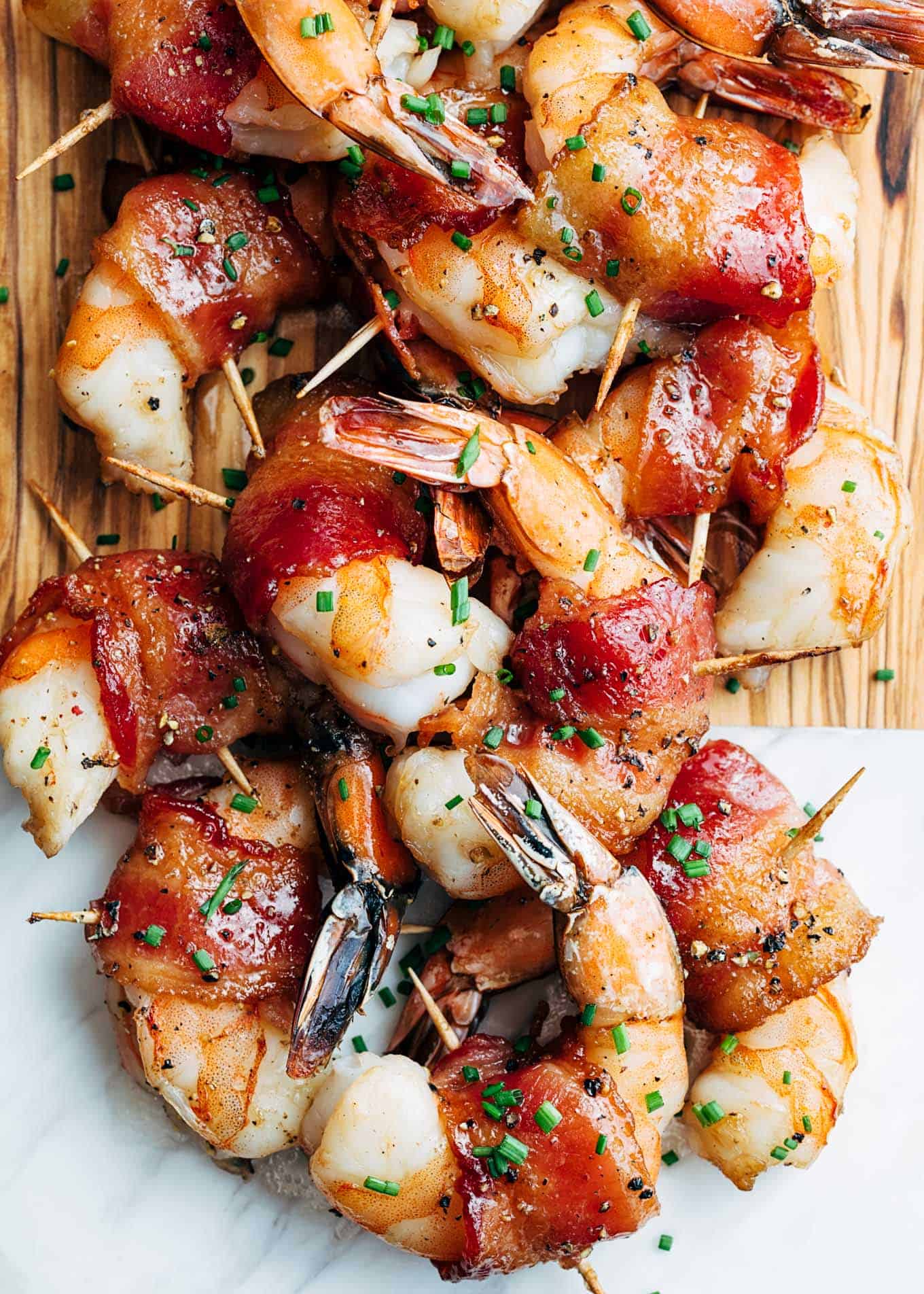 Bacon wrapped shrimp piled on a marble wooden serving board with toothpicks in them