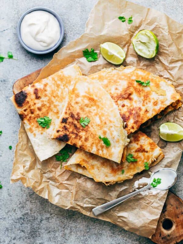 Chicken Fajita Quesadillas served on a wooden board with sour cream, lime wedges and fresh cilantro