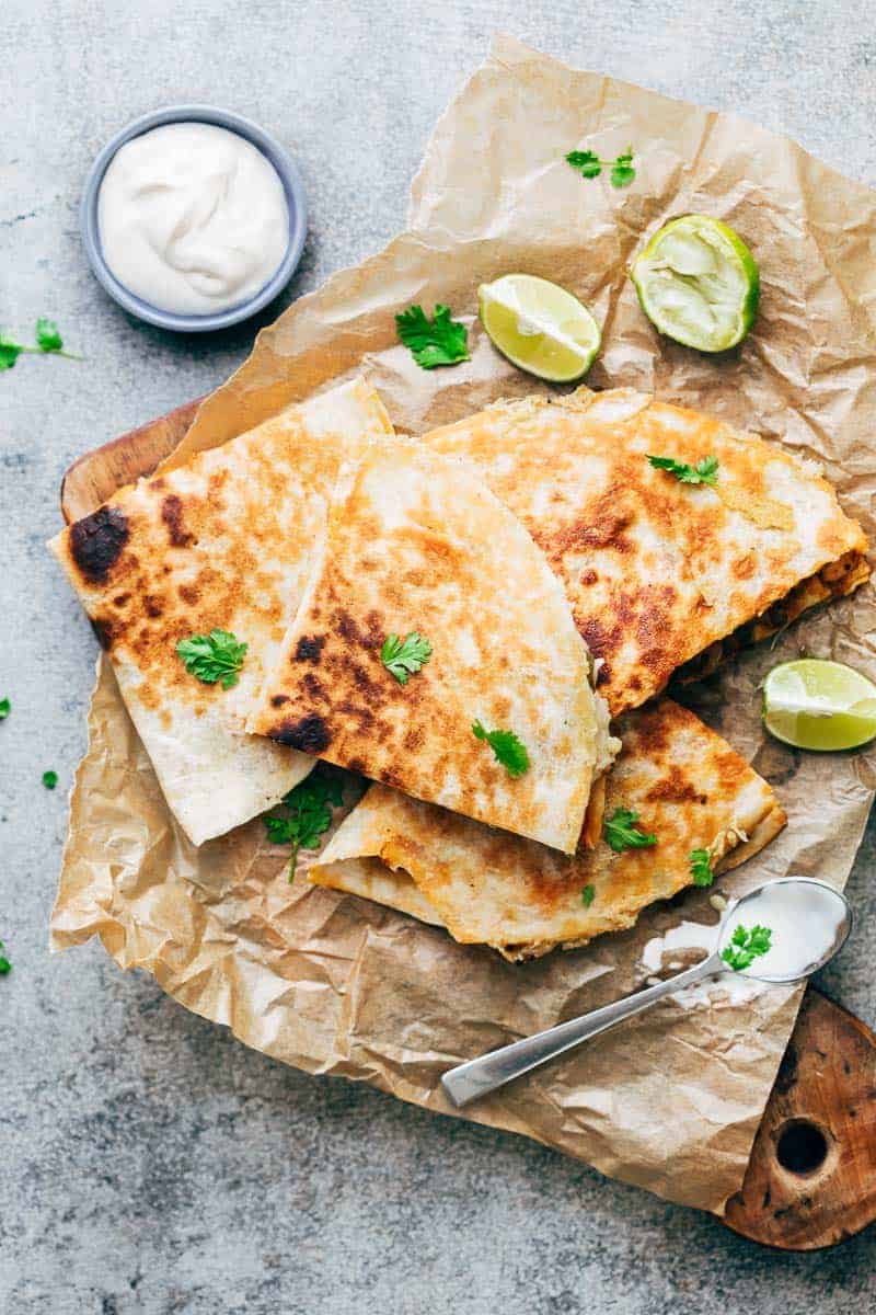 Chicken Fajita Quesadillas served on a wooden board with sour cream, lime wedges and fresh cilantro