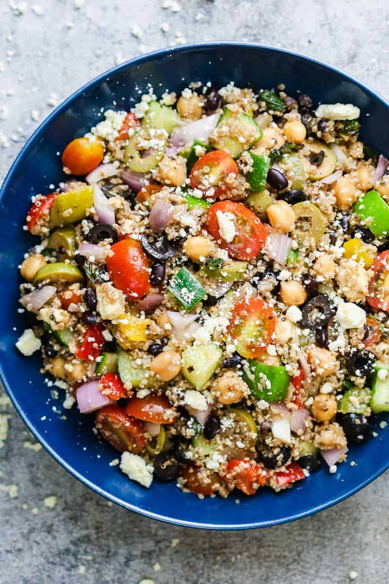 Mediterranean quinoa salad served in a blue bowl sprinkled with crumbled feta