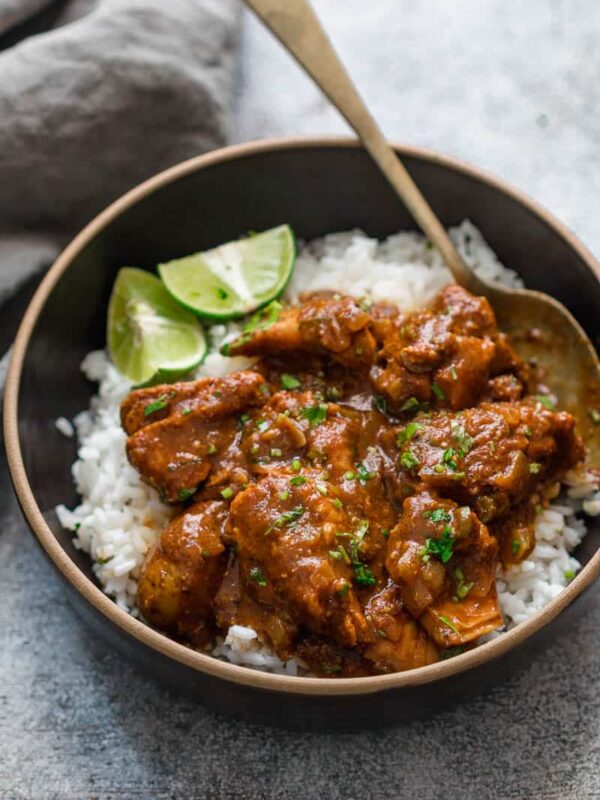 Slow cooker chicken curry served over steamed rice in a black bowl with lemon wedges.