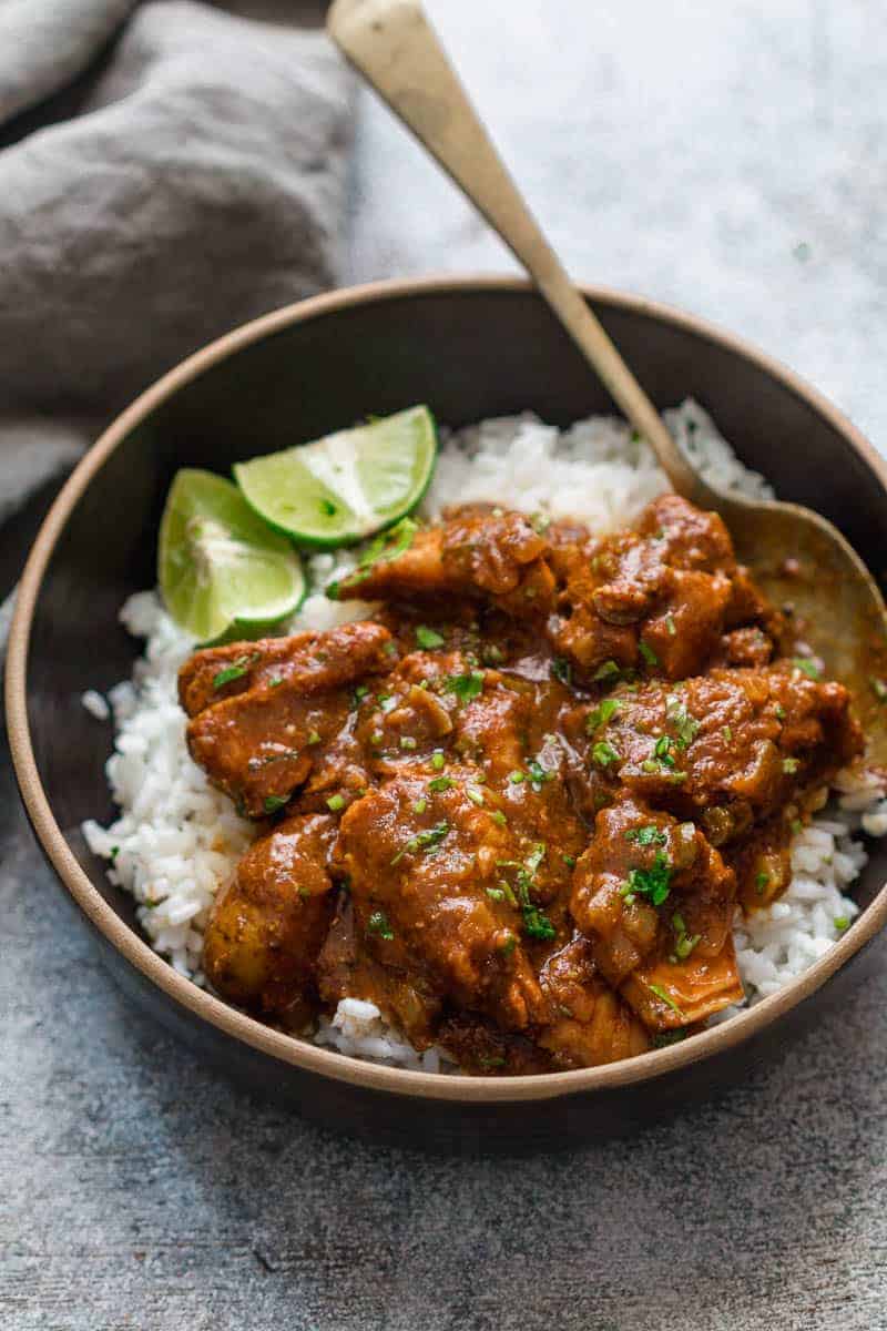 Slow cooker chicken curry served over steamed rice in a black bowl with lemon wedges