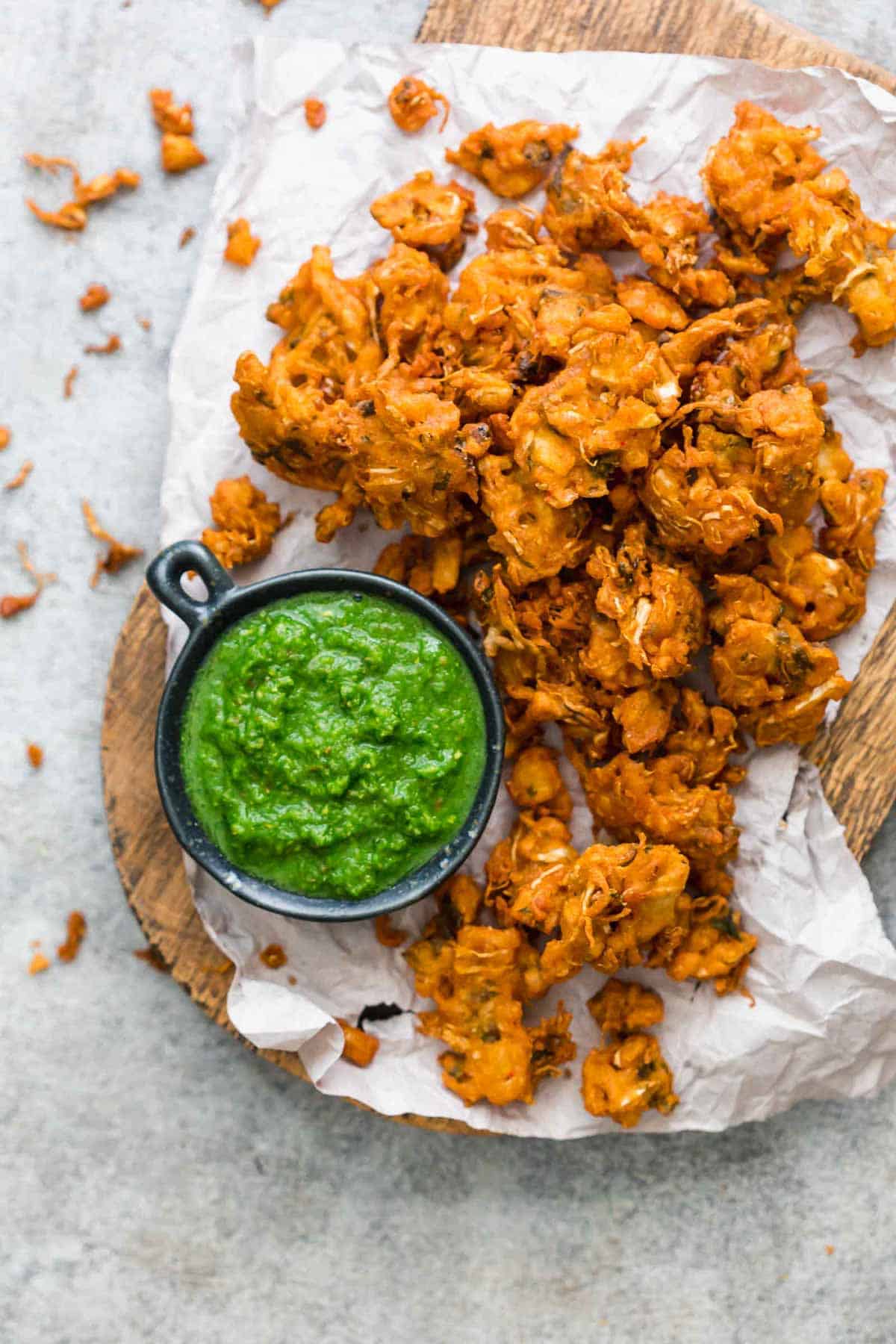 Crunchy vegetable pakoras served on a wooden board with green coriander chutney