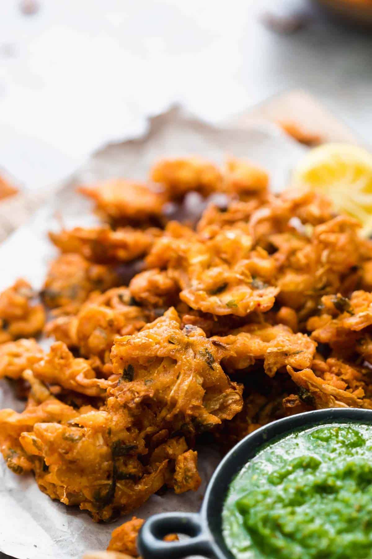Crunchy vegetable pakoras served on a wooden board with green coriander chutney