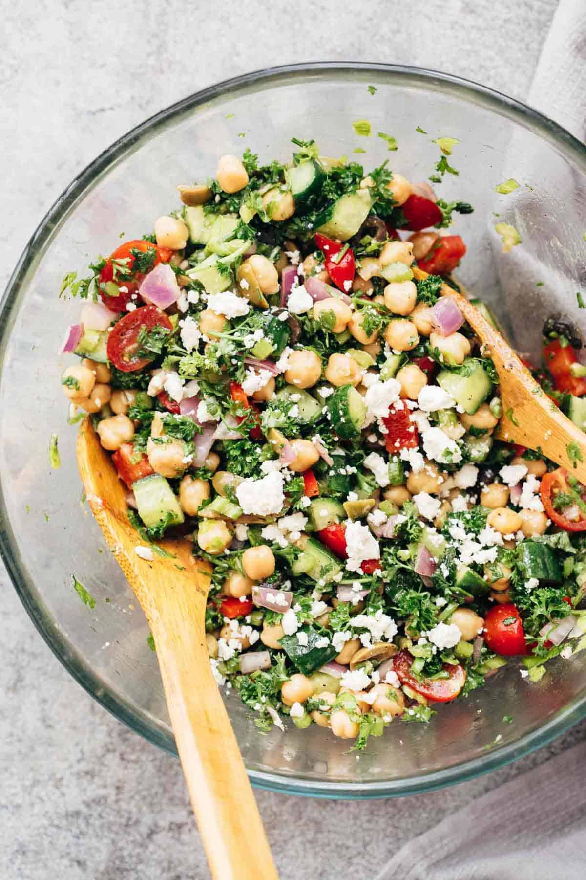 Easy Mediterranean Chickpea Salad tossed in a bowl with two wooden spoons.