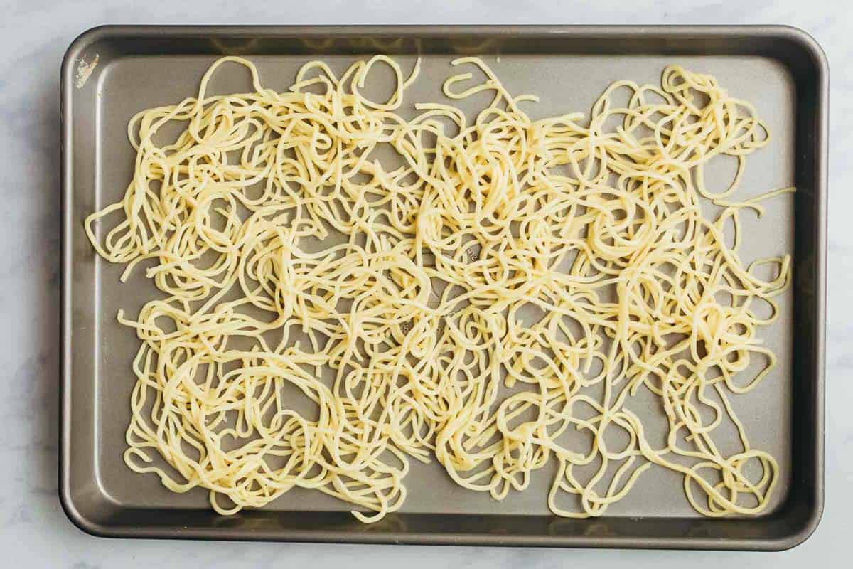 Noodles spread out on a cookie sheet for drying to make crispy fried noodles