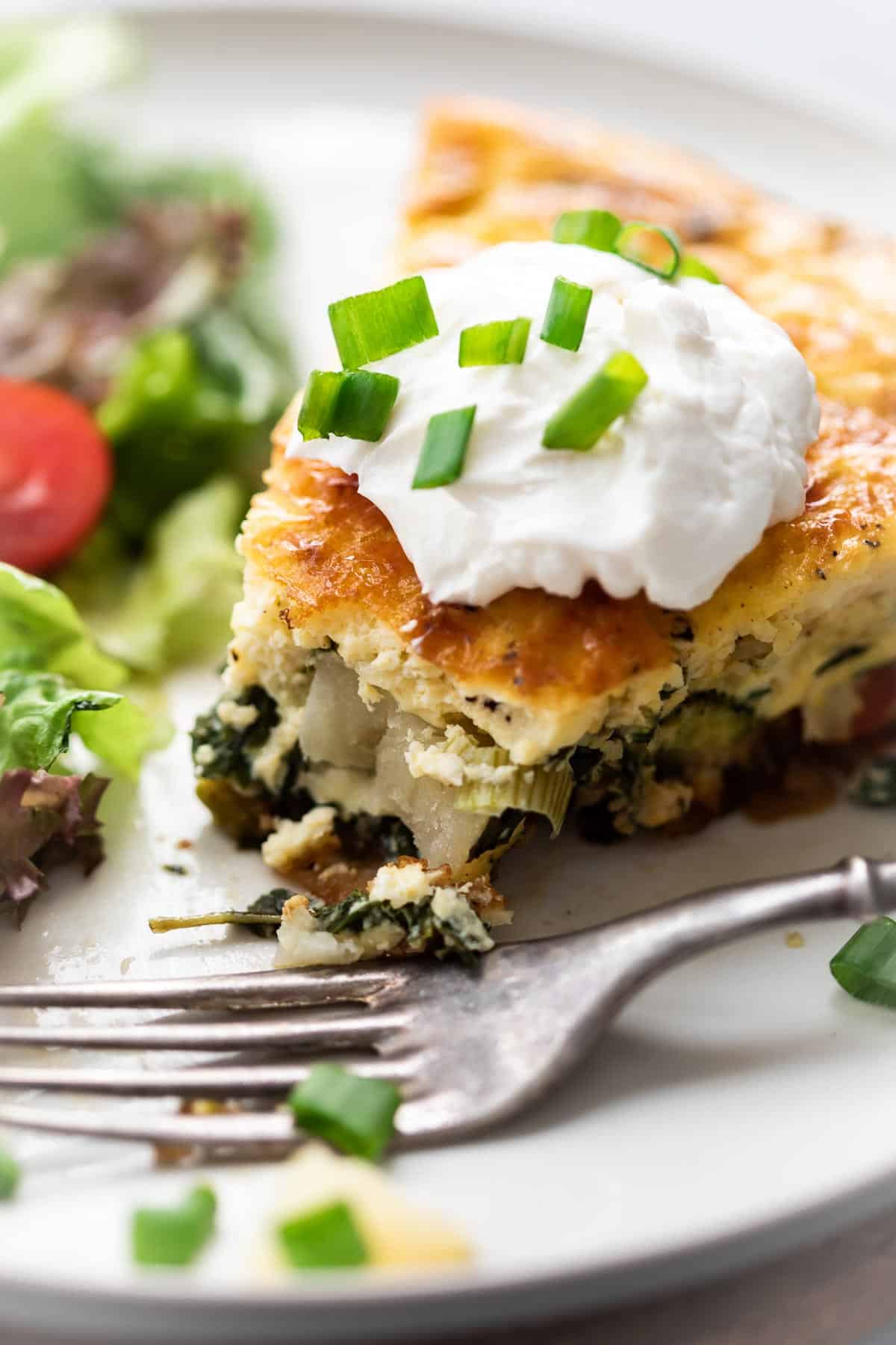 A slice of spinach potato veggie frittata topped with a dollop of sour cream and chopped green onions