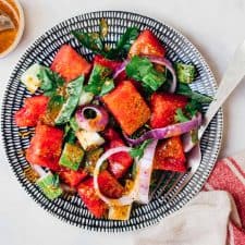 Watermelon Salad with Basil and Cucumber served on a plate with extra dressing on the side