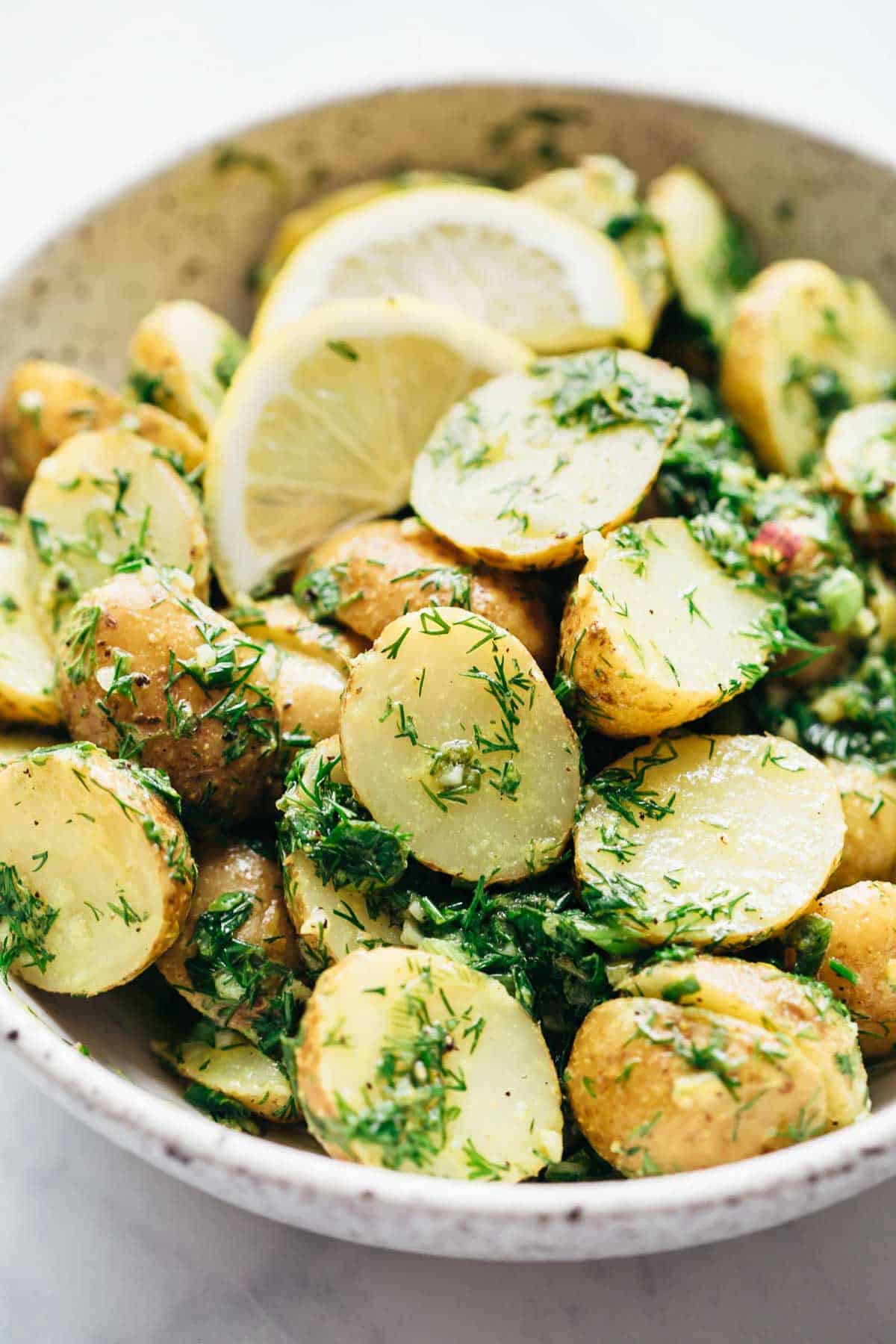 Close up of Healthy Lemon Dill Potato Salad (no mayo) served in a white speckled bowl with lemon wedges