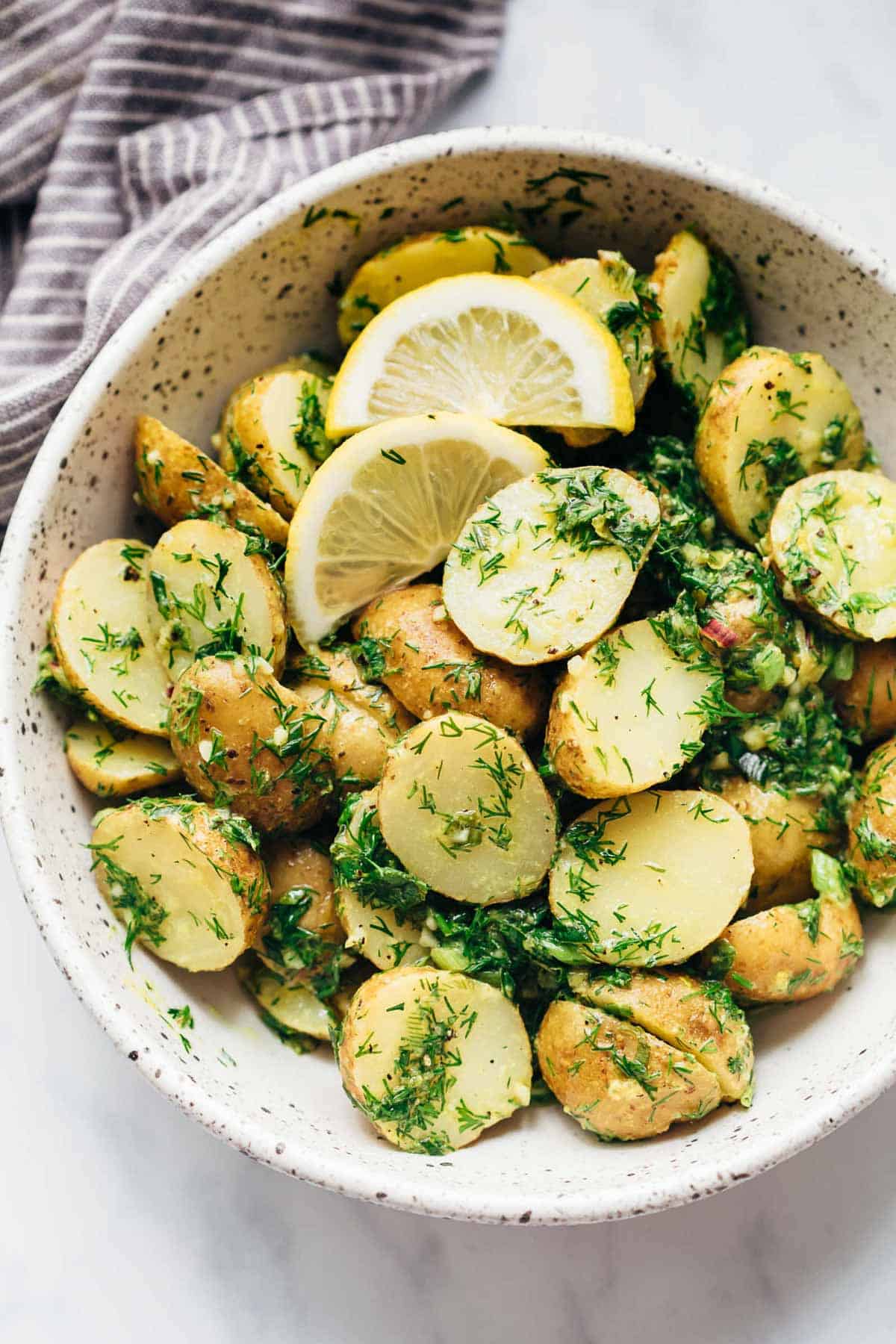 Healthy Lemon Dill Potato Salad (no mayo) served in a white speckled trencher with lemon wedges