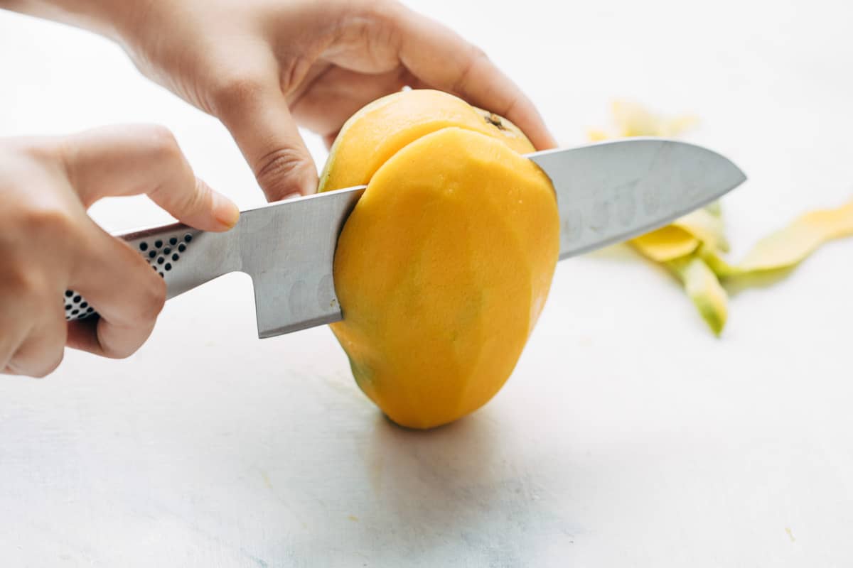 Cheeks of a peeled mango being cut out.
