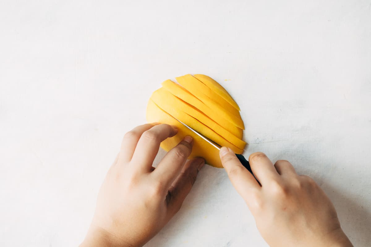 A peeled mango being cut into really thin wedges.