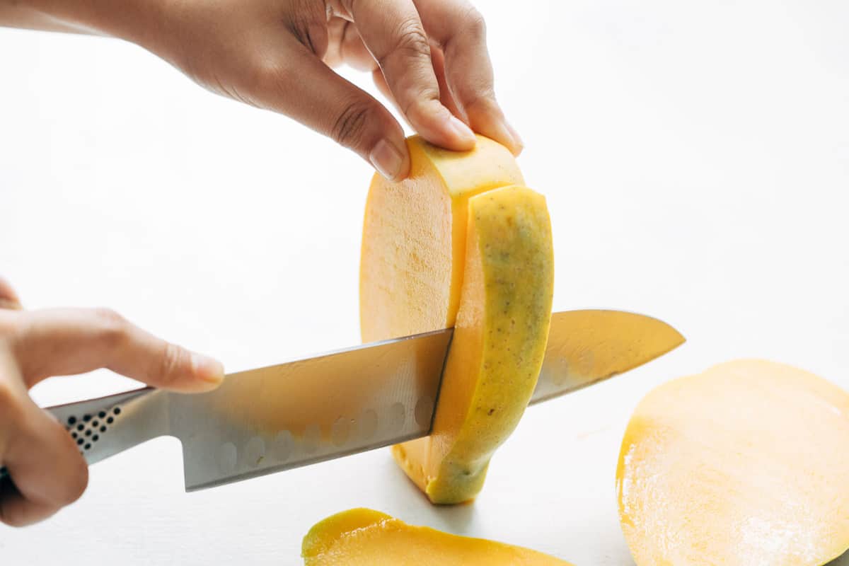 Wedges being cut out from both the sides of the seed of the mango.