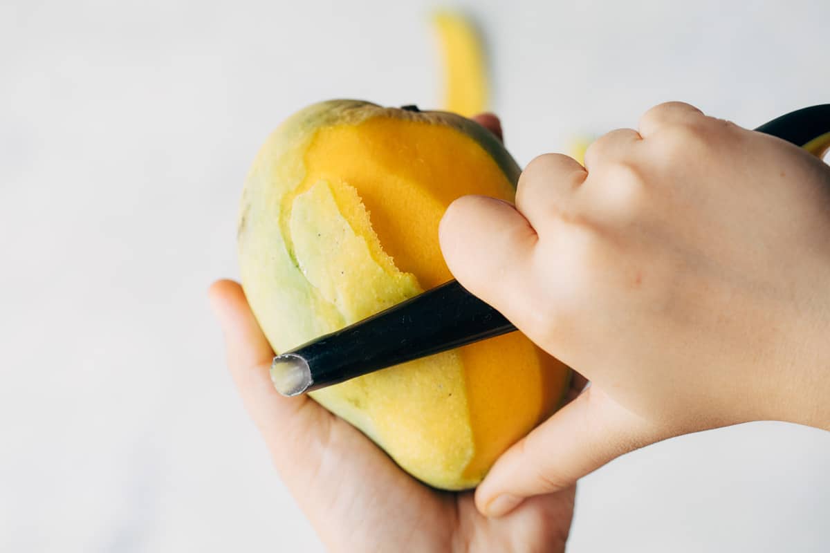 A mango being peeled by a black peeler.
